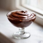 A serving of rich, dark homemade chocolate pudding swirled high in a clear glass dessert dish.