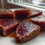 Five thick slices of perfectly Seared Ahi Tuna, crusted with sesame seeds, resting on a white plate.