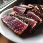 Slices of perfectly cooked Seared Ahi Tuna, showing a deep red center and a dark, peppery crust, served on a white plate.