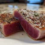 Two thick slices of seared tuna steak, showing a deep pink rare center and a heavily seasoned crust, perfect for MARINADE FOR TUNA STEAK.