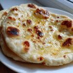 Close-up of two pieces of soft, freshly cooked naan bread brushed with melted butter, showing charred spots.