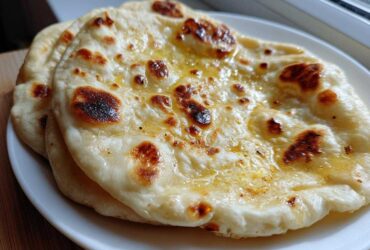 Close-up of two pieces of soft, freshly cooked naan bread brushed with melted butter, showing charred spots.