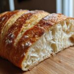 Close-up of a freshly baked french bread loaf showing the golden crust and airy interior crumb structure.