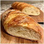 Close-up of a freshly baked french bread loaf, sliced open to show the soft, airy interior crumb and golden crust.