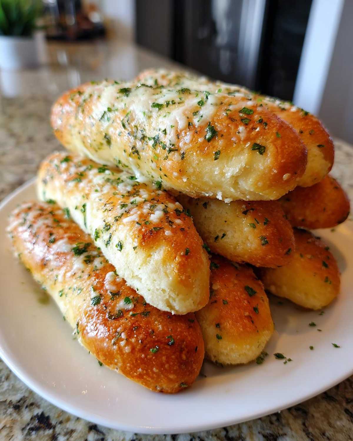 A stack of soft, golden brown garlic cheese breadsticks topped with melted cheese and parsley on a white plate.
