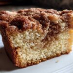 Close-up of a moist slice of sour cream coffee cake showing the crumb and rich cinnamon swirl topping.
