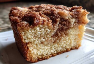 Close-up of a moist slice of sour cream coffee cake showing the crumb and rich cinnamon swirl topping.