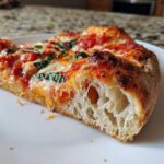 Close-up of a slice of pizza showing the airy, open crumb structure of the sourdough discard pizza dough.