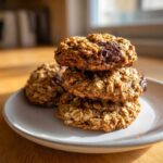 A stack of three thick, chewy oatmeal cookie treats with melted chocolate chips, sitting on a light gray plate.