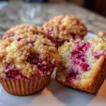 Close-up of delicious strawberry muffins with a crumb topping, one cut open showing the bright red fruit inside.