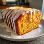 Close-up of a slice of moist sweet potato pound cake topped with white glaze and orange zest.