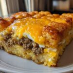 A square slice of tater tot breakfast casserole featuring layers of crispy tater tots, sausage, and melted cheddar cheese.