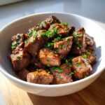 Close-up of tender crockpot steak bites coated in sauce and sprinkled with fresh chopped parsley in a white bowl.
