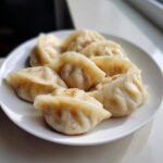 A plate of freshly steamed Traditional Chinese Dumplings with slightly browned bottoms, ready to eat.