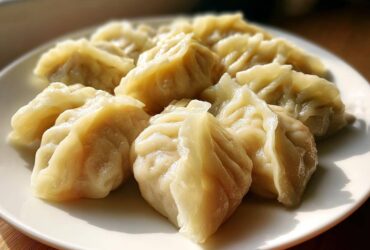 A close-up of several freshly steamed Traditional Chinese Dumplings arranged on a white plate.