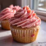 Close-up of a perfectly baked strawberry cupcake topped with thick, pink strawberry frosting swirls.