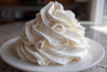 A tall, perfectly piped swirl of white vanilla buttercream frosting sitting on a small white plate.