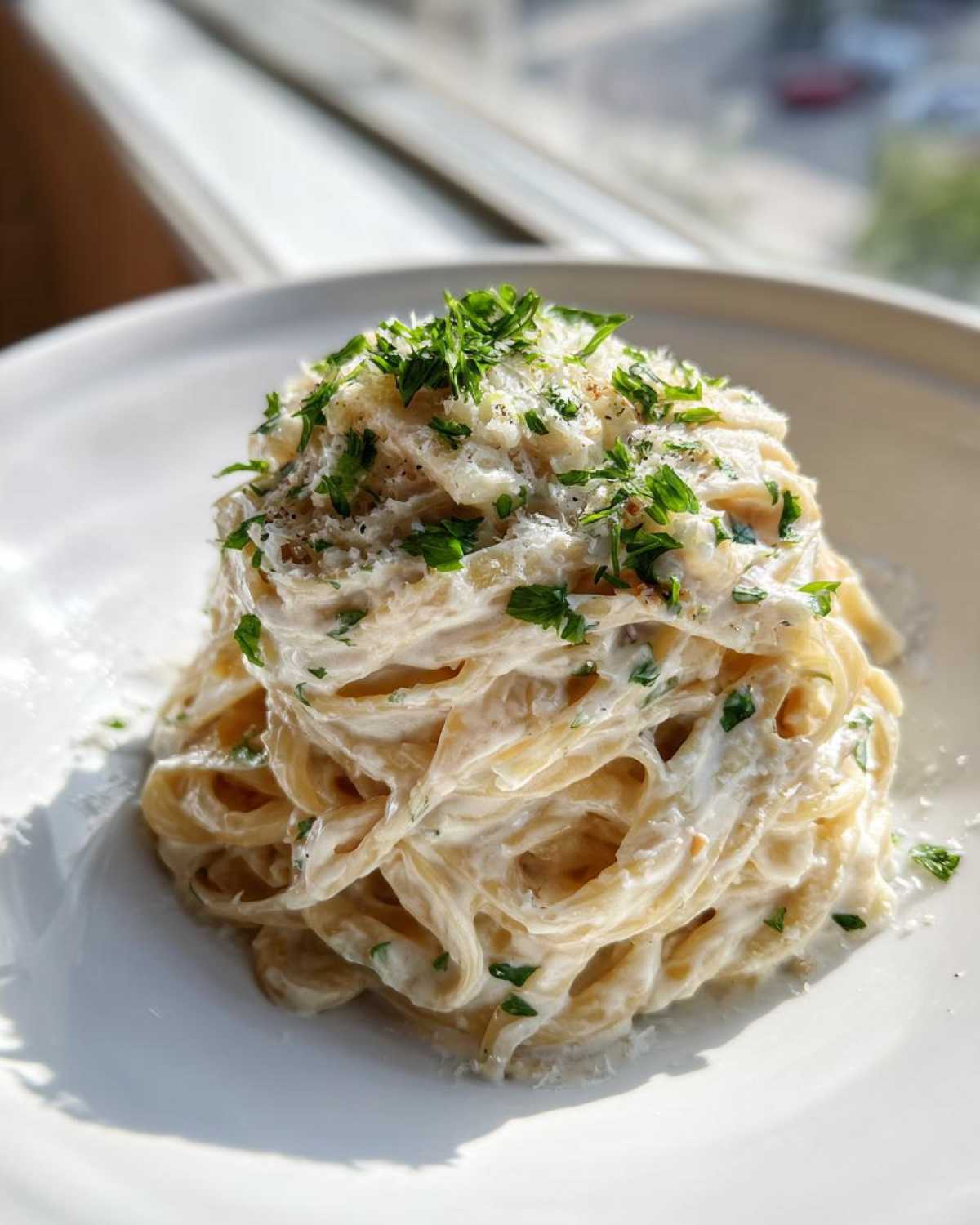 A tall swirl of creamy pasta coated in a rich sauce, topped with grated cheese and fresh parsley for the garlic parmesan pasta.