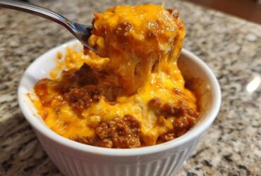 A spoonful of hot chili cheese dip being lifted from a white bowl, showing melted, stringy cheddar cheese.
