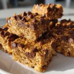A stack of homemade, chewy protein bars loaded with oats and topped with melted chocolate chips.