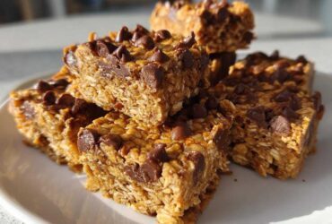 A stack of homemade, chewy protein bars loaded with oats and topped with melted chocolate chips.