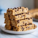 A stack of homemade, chewy protein bars loaded with oats and mini chocolate chips on a white plate.