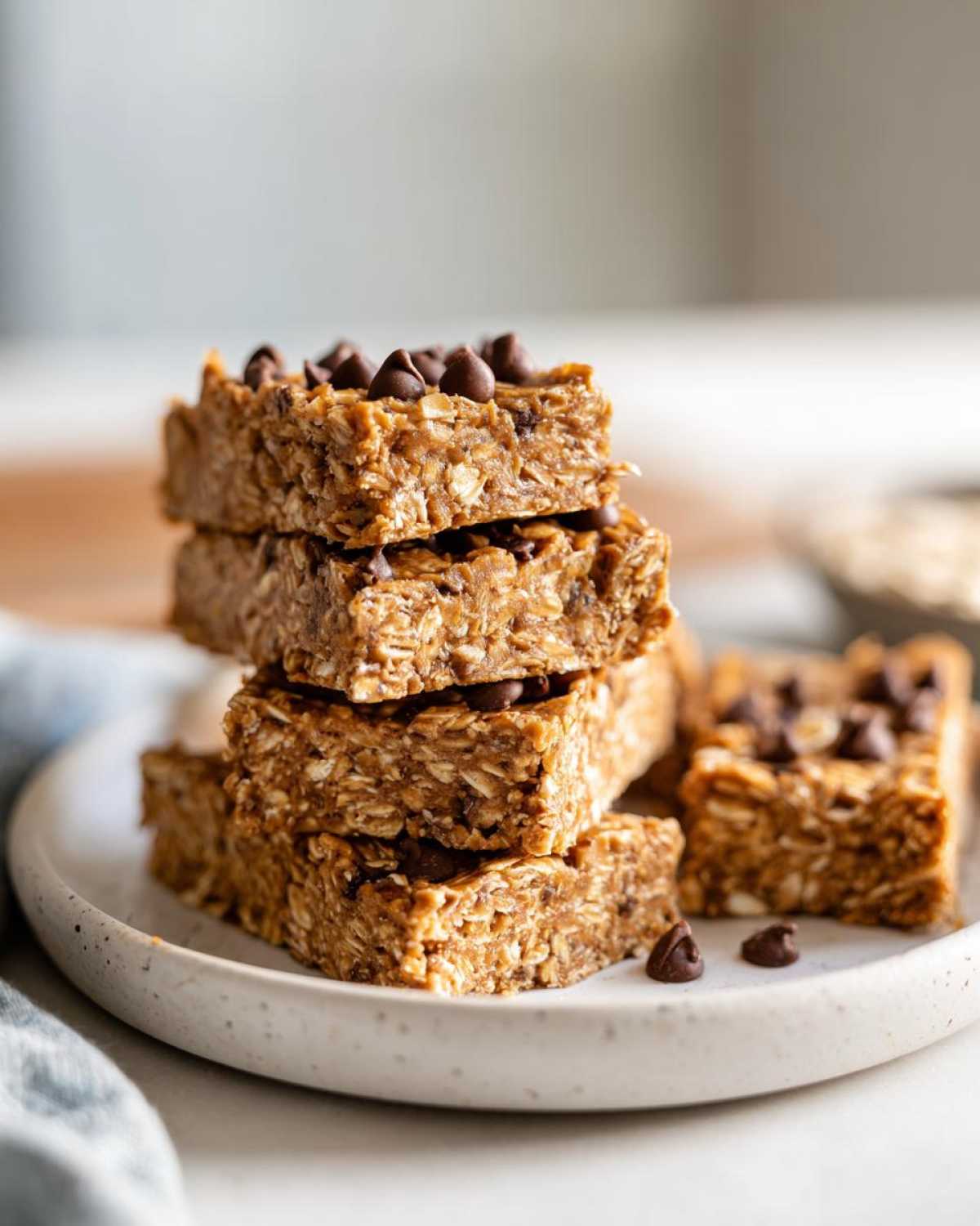 A stack of four homemade, chewy protein bars topped with mini chocolate chips on a speckled white plate.