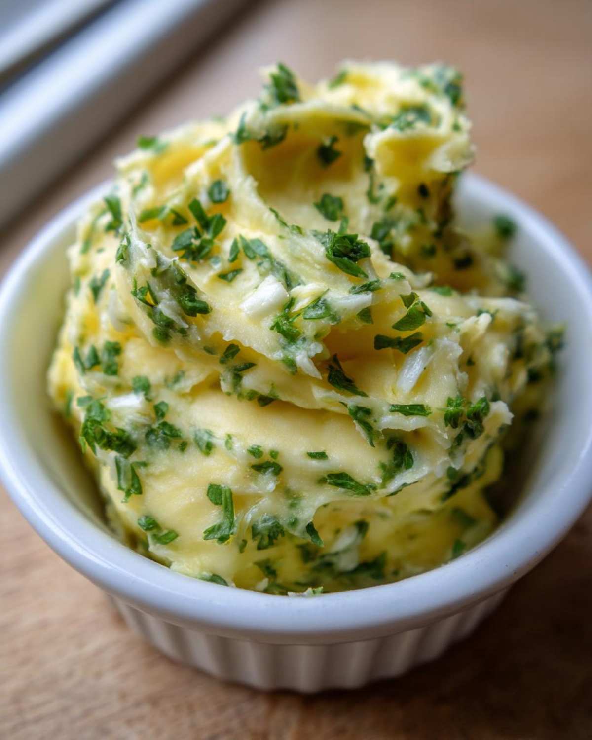 Close-up of fluffy homemade garlic butter mixed with fresh green herbs, served in a small white ramekin.