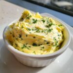 Close-up of creamy, whipped garlic butter mixed with chopped green herbs, served in a white ramekin.