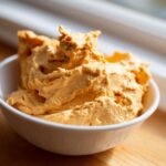 A close-up shot of creamy, orange pumpkin fluff dessert served in a small white bowl.