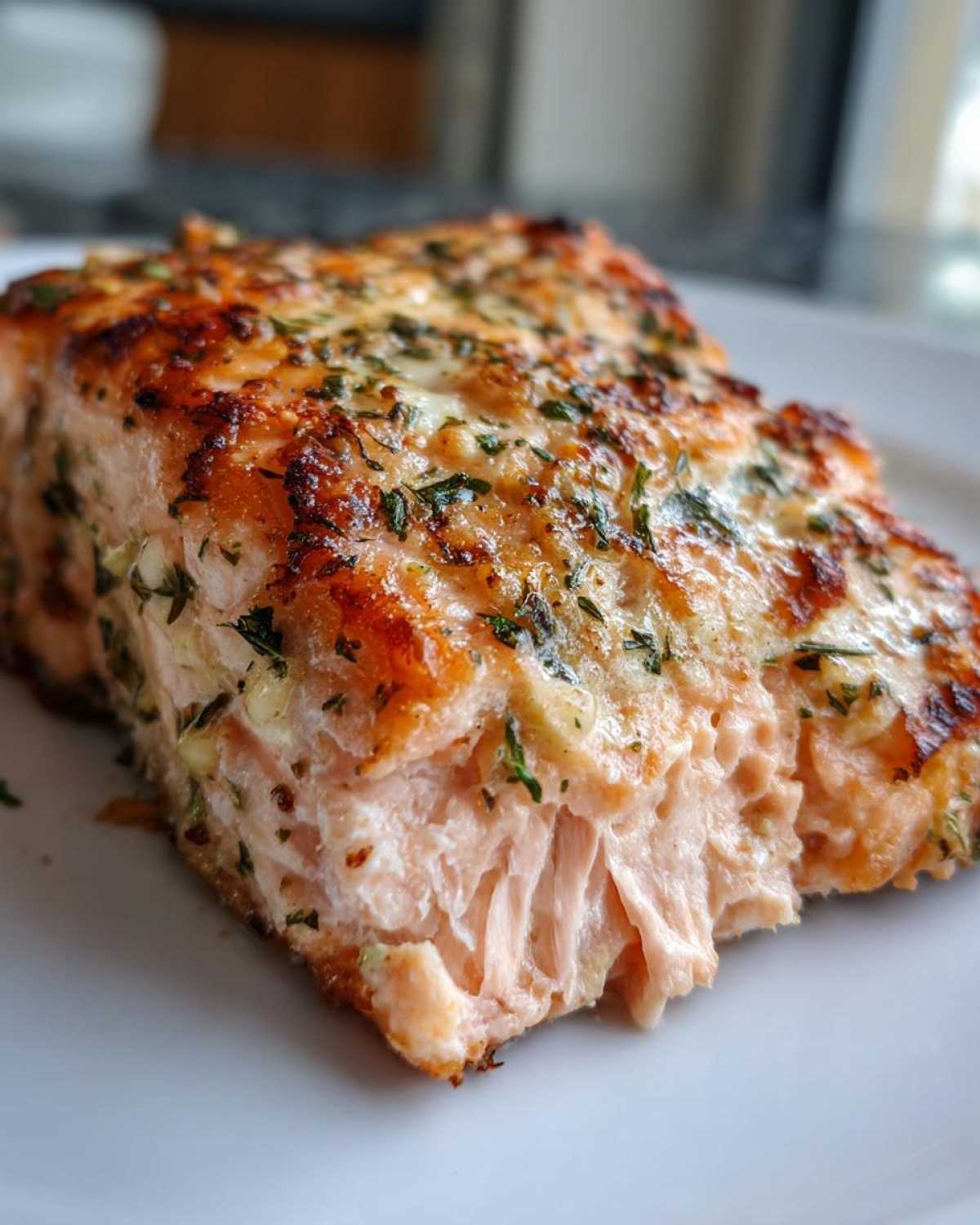 Close-up of a flaky, perfectly cooked piece of air fryer salmon topped with herbs and browned seasoning.