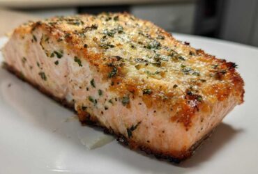 Close-up of a golden-brown, seasoned air fryer salmon fillet resting on a white plate.
