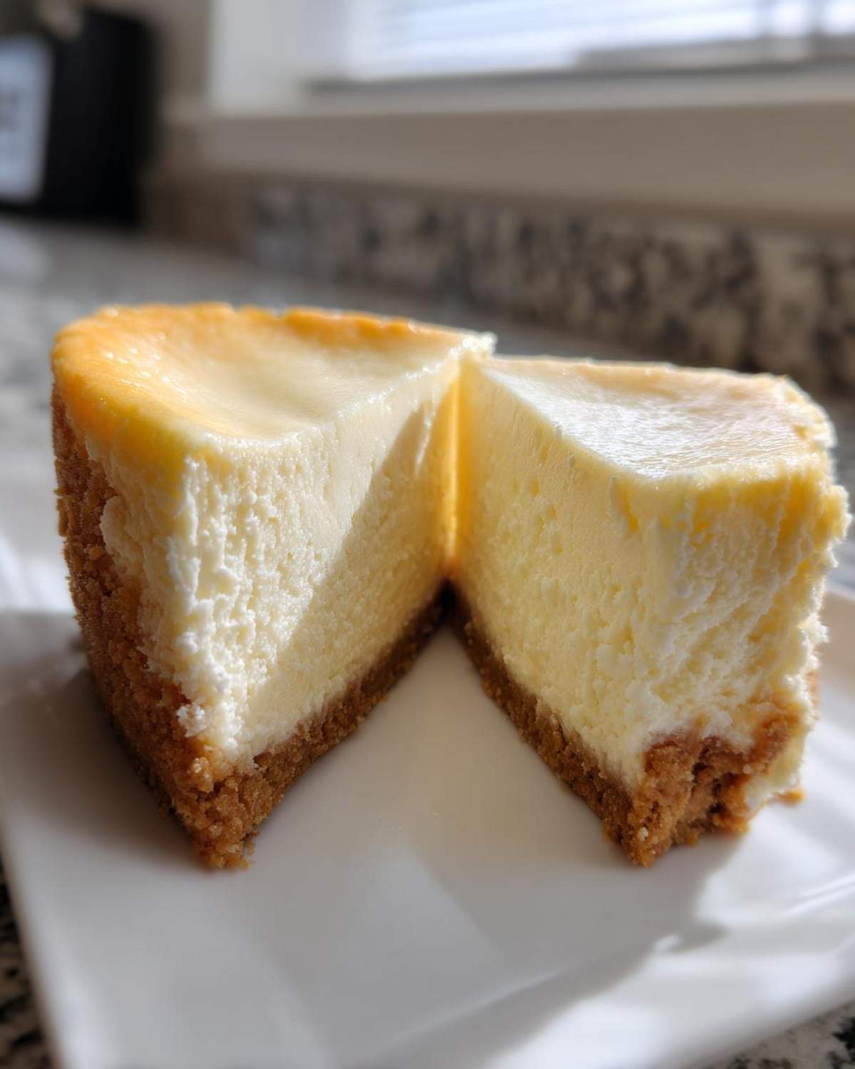 Two creamy slices of baked cheesecake with a thick graham cracker crust, showcasing the texture of this cheesecake recipe.