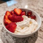 A bowl of creamy fruit dip served with fresh sliced strawberries and red grapes, perfect for a quick fruit dip snack.
