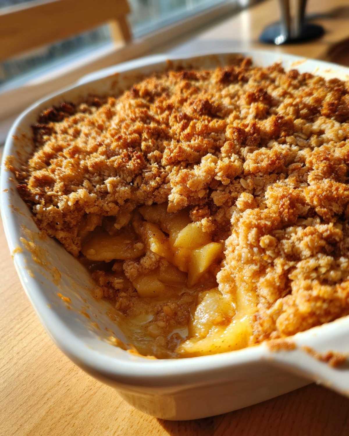 Close-up of a portion scooped out of a freshly baked apple crisp recipe, showing warm, gooey apples under a crunchy oat topping.