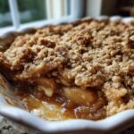 Close-up view of a freshly baked apple crumble showing the gooey, spiced apple filling beneath a thick, crunchy oat topping.