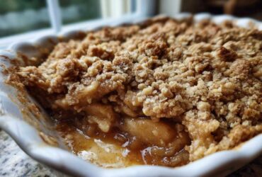 Close-up view of a freshly baked apple crumble showing the gooey, spiced apple filling beneath a thick, crunchy oat topping.