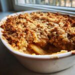 A close-up view of a freshly baked apple crumble with a thick, golden-brown, crunchy topping and soft apple filling visible.