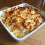 Close-up of a baked corn dip in a white square dish, featuring a bubbly, golden-brown melted cheese crust.