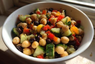 Close-up of a vibrant bean salad featuring chickpeas, black beans, cucumber, and bell peppers in a white bowl.
