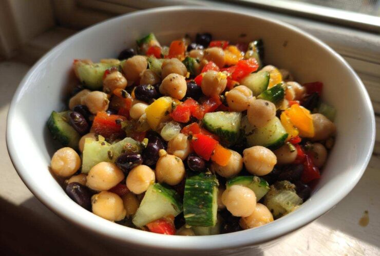 Close-up of a vibrant bean salad featuring chickpeas, black beans, cucumber, and bell peppers in a white bowl.