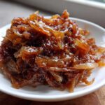 Close-up of deeply rich, glossy caramelized onions piled high on a small white dish.