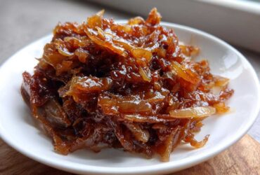 Close-up of deeply rich, glossy caramelized onions piled high on a small white dish.