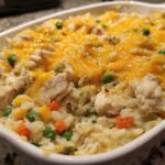 Close-up of creamy chicken and rice casserole topped with melted cheddar cheese and mixed vegetables.