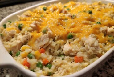 Close-up of creamy chicken and rice casserole topped with melted cheddar cheese and mixed vegetables.