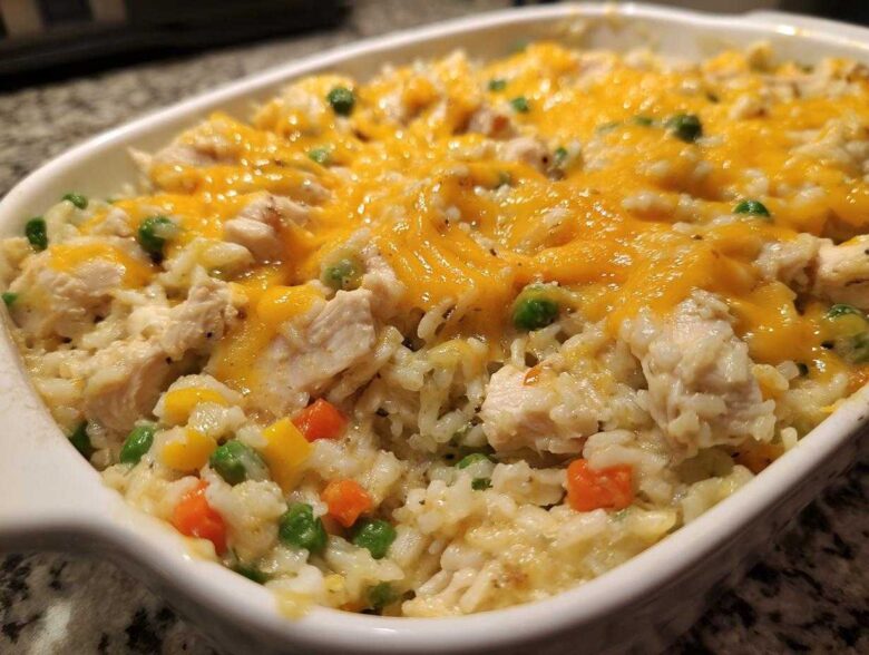 Close-up of creamy chicken and rice casserole topped with melted cheddar cheese and mixed vegetables.