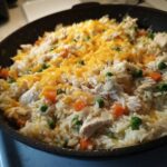 Close-up of creamy chicken and rice mixed with peas and carrots, topped with melted cheddar cheese.