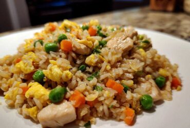 Close-up of a plate piled high with homemade chicken fried rice featuring scrambled egg, carrots, and peas.