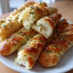 A pile of golden, soft copycat breadsticks seasoned with garlic and parsley on a white plate.
