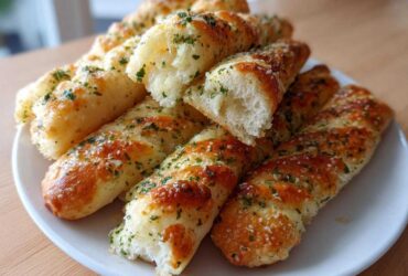 A pile of golden, soft copycat breadsticks seasoned with garlic and parsley on a white plate.